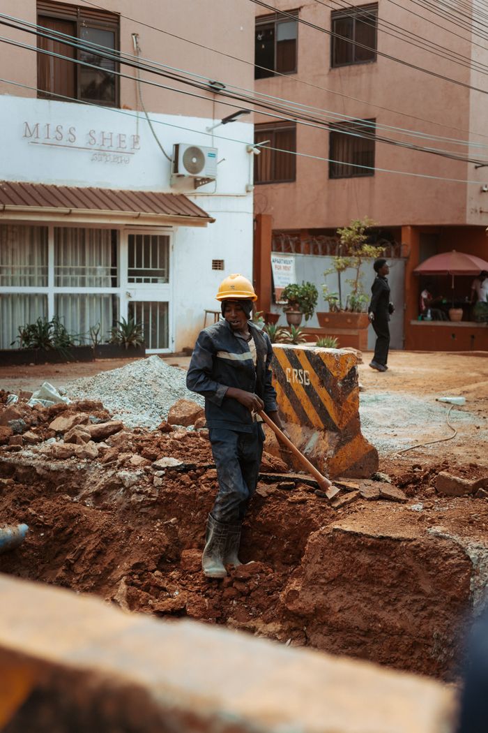 A construction worker digs at an urban site in front of buildings, showcasing urban development.