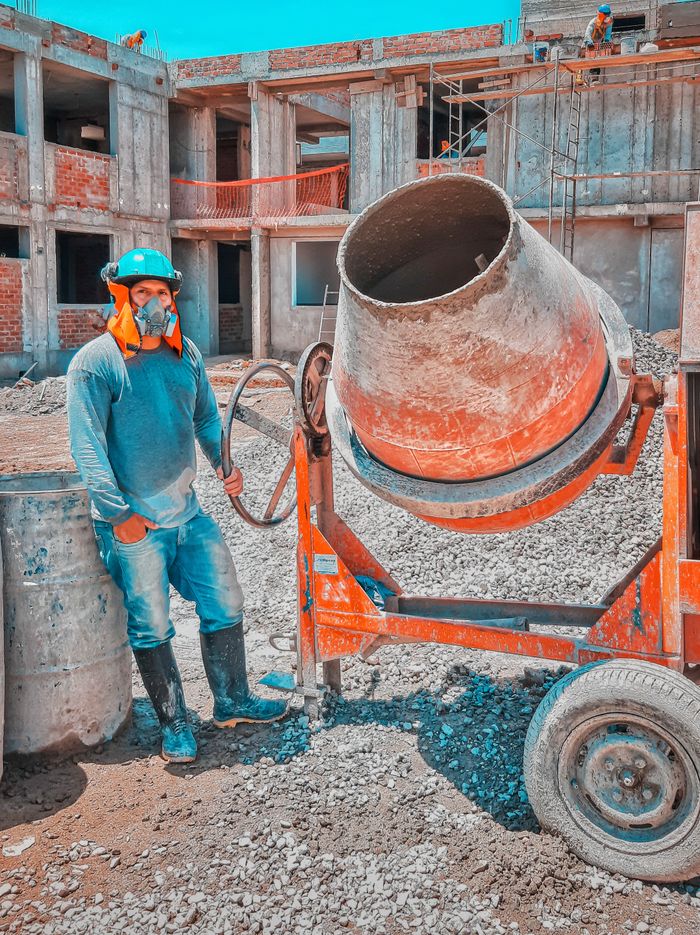Construction worker operates heavy concrete mixer on sunny outdoor site.