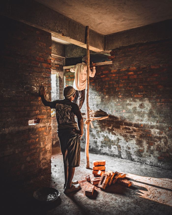 Two men working inside a rustic brick building, illuminated by sunlight, showcasing construction labor.